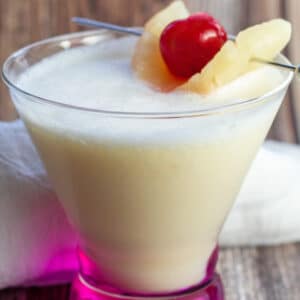 Cocktail chi chi dans un verre à cocktail avec garniture d'ananas et de cerise au marasquin.