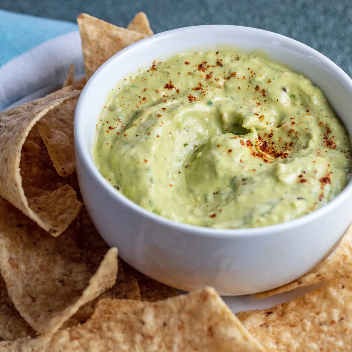 Guacamole in a white bowl surrounded by tortilla chips.