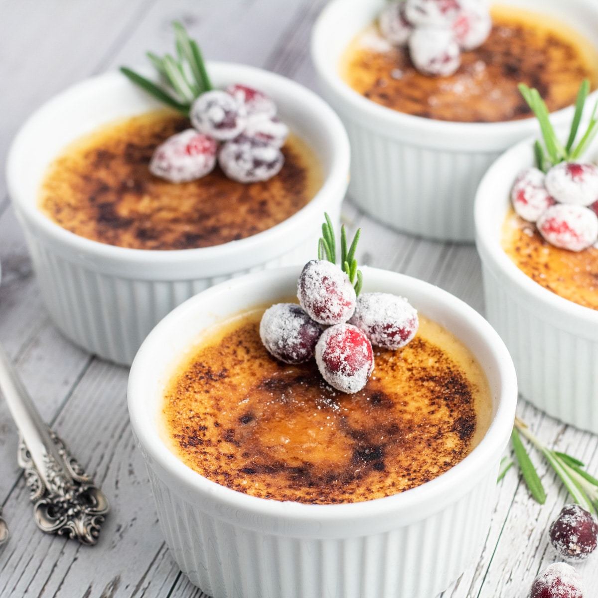 Toasted eggnog creme brulee in ramekins with sugared cranberries and a sprig of rosemary.