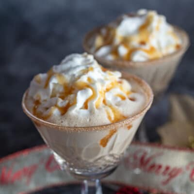 Gingerbread eggnog cocktail served in crystal glasses with whipped cream and syrup drizzle.