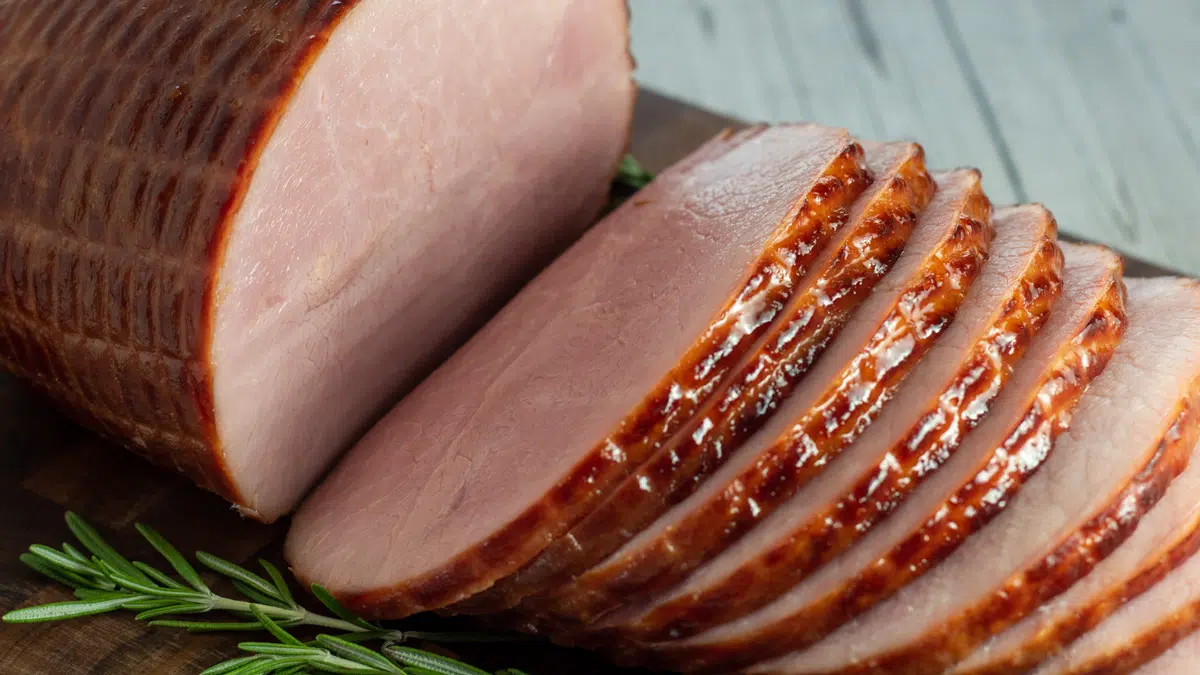 Horizontal image of sliced ham on a wooden cutting board.