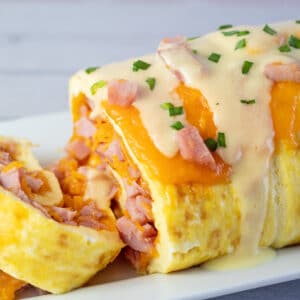 Rouleau d'omelette ou roulade de petit-déjeuner au jambon et au fromage servie sur une assiette blanche.