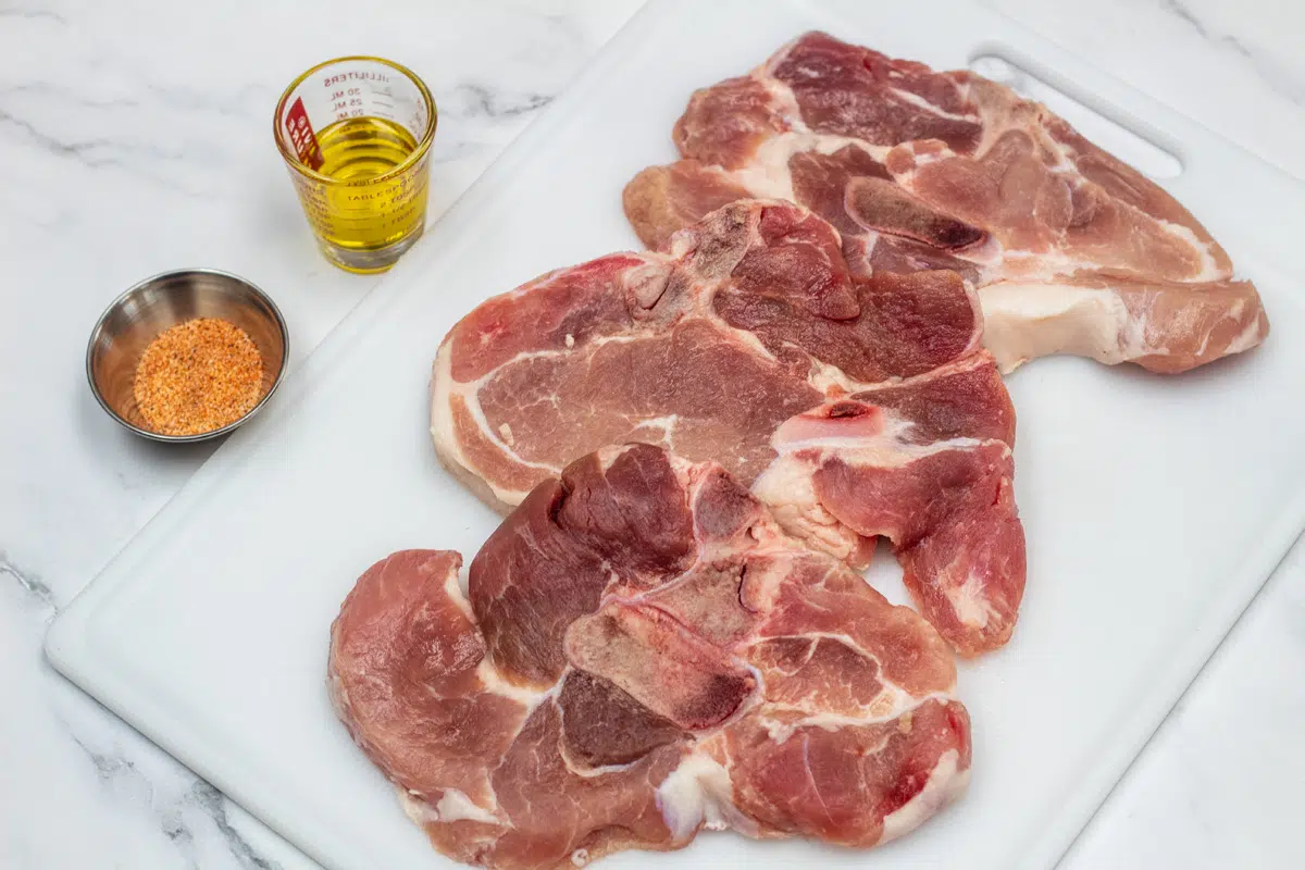Ingredient photo showing pork steaks, seasoning, and olive oil.