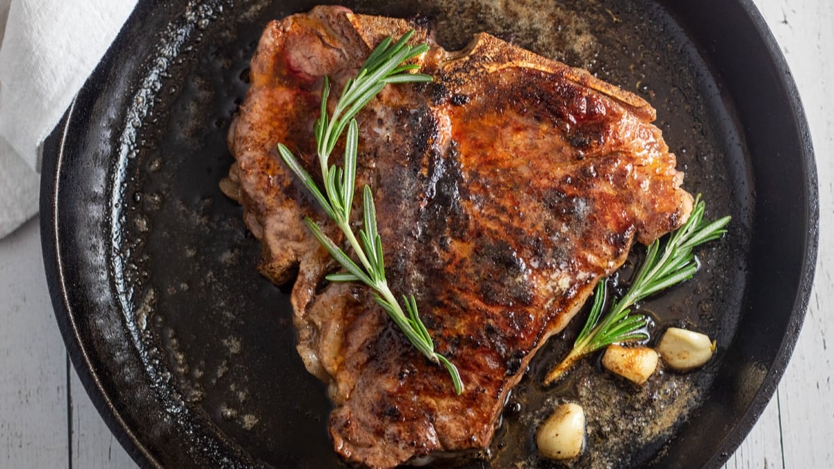Closeup lebar pada panci steak t-bone yang dipanggang dalam wajan besi cor.