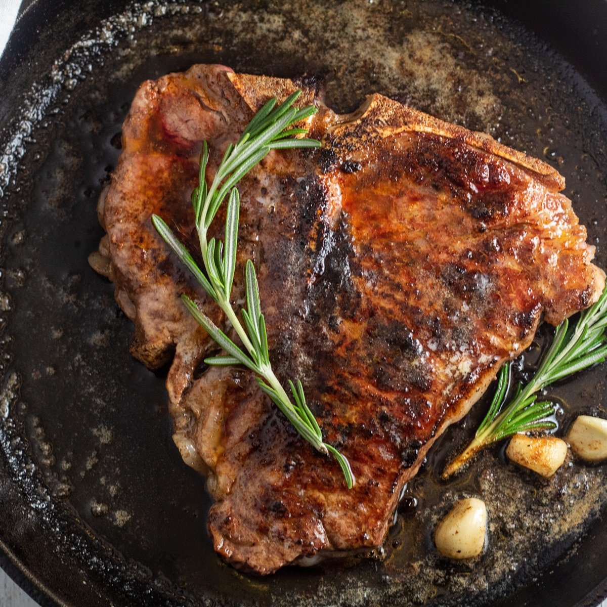 Pan seared t-bone steak in pan with garlic and rosemary.
