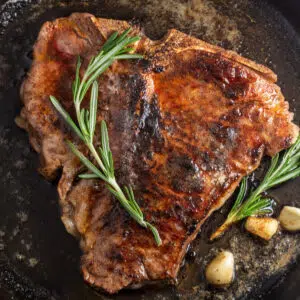 Closeup on the pan seared t-bone steak in pan with garlic and rosemary.