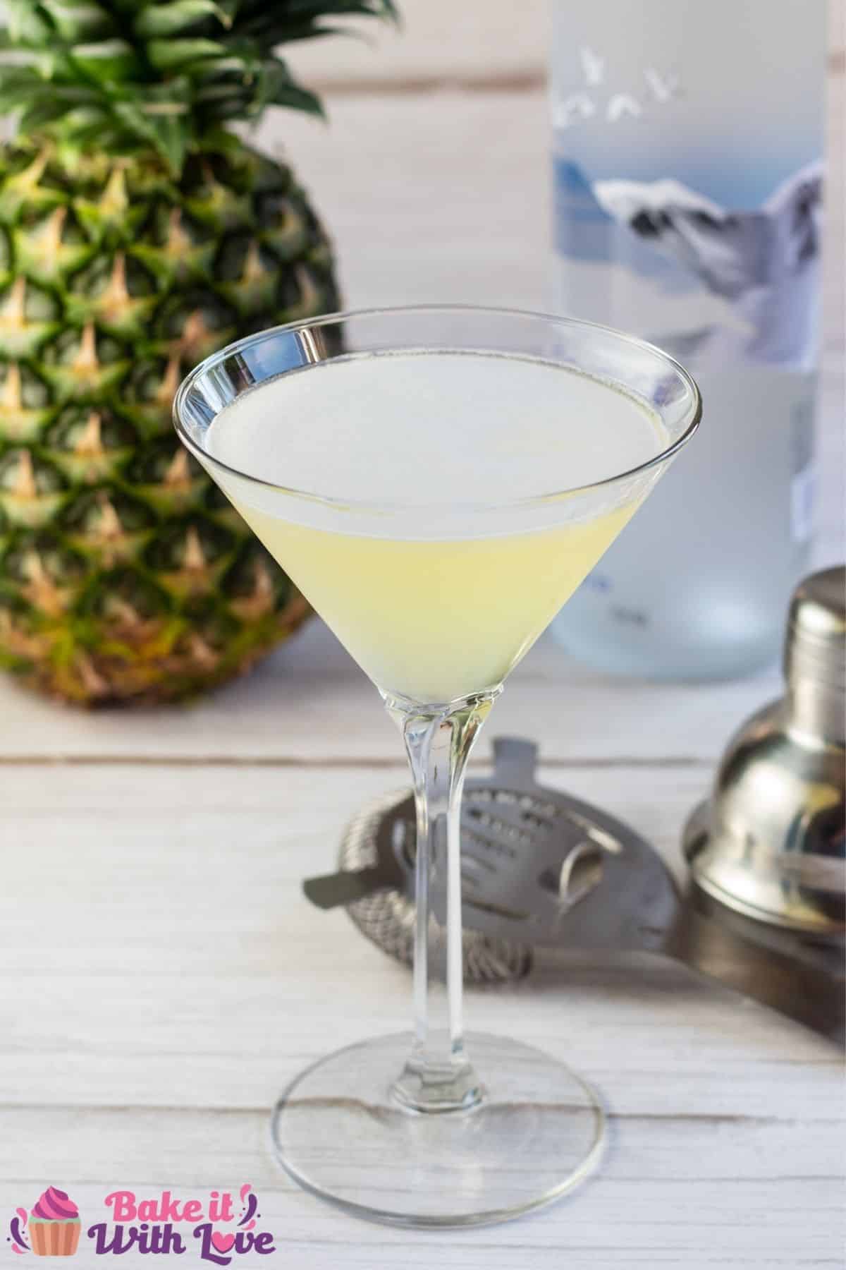 Tall close up image of pineapple martini with fresh pineapple behind.