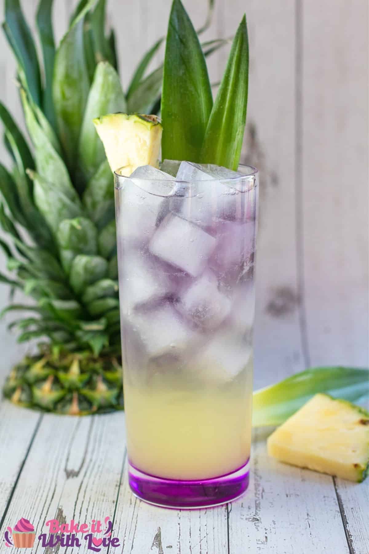 Tall image of the Royal Hawaiian cocktail served with pineapple top in background.
