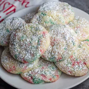 Square image of sprinkle Christmas cookies on a white plate with a grey background.