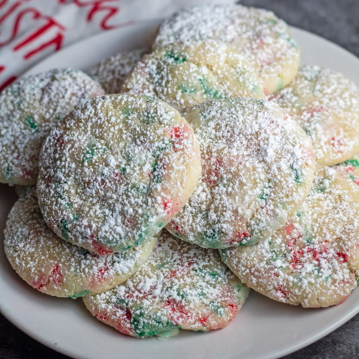 Imagen cuadrada de espolvorear galletas de Navidad en un plato blanco con un fondo gris.