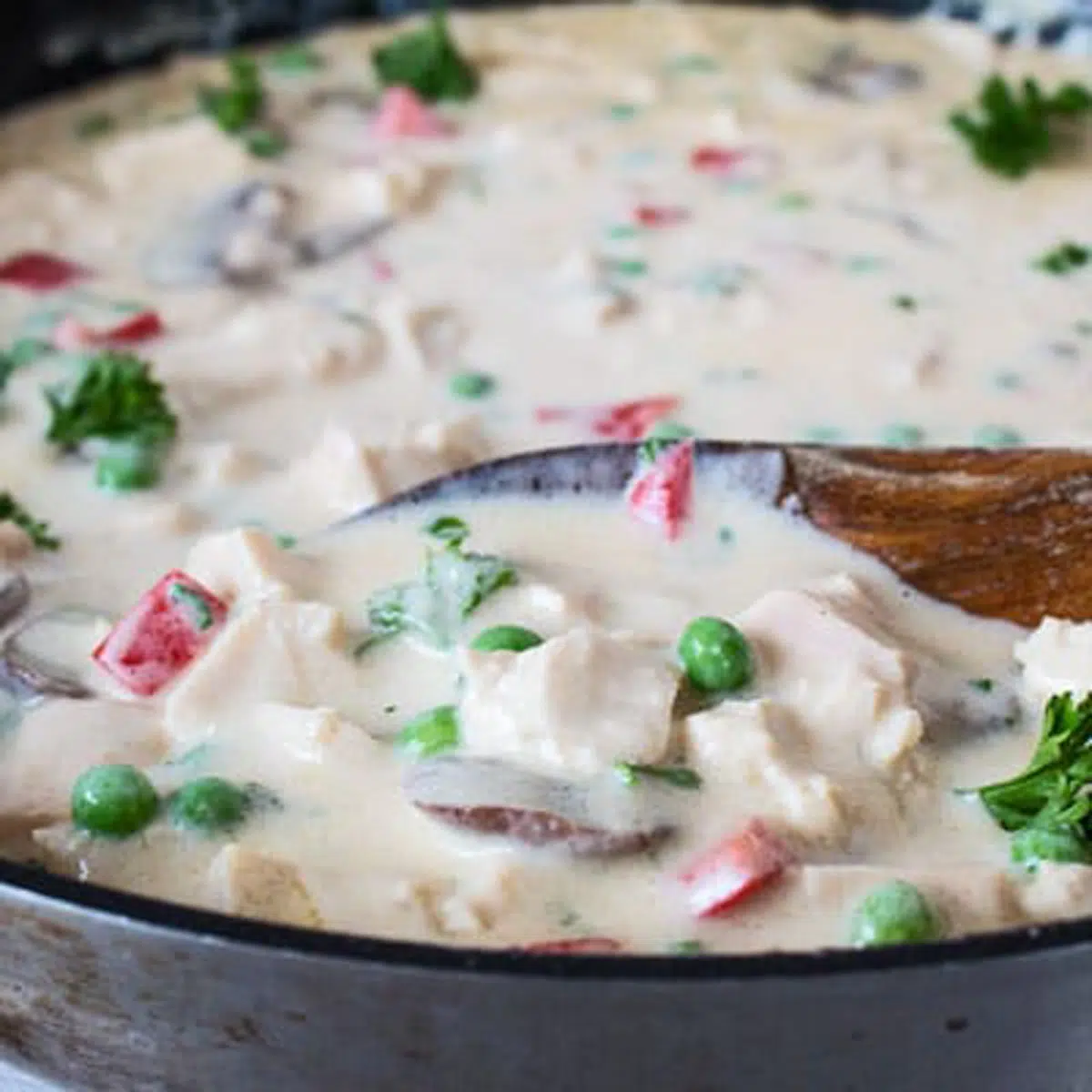 Square image of chicken a la king in a skillet with wooden spoon.