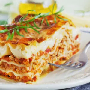 Square image of the sliced meat lasagna with red sauce on white plate.