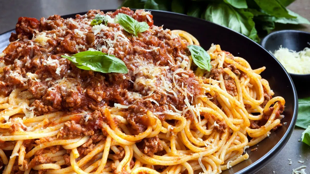 Wide image of the plated spaghetti bolognese with greens in the background.