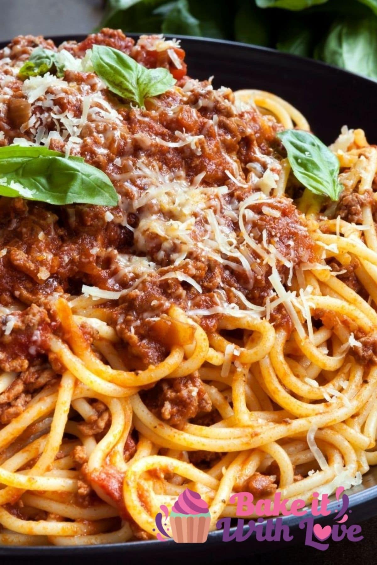 Tall closeup on the plated spaghetti bolognese topped with freshly grated Parmesan and basil leaves.