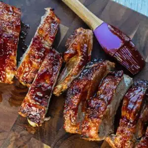 Square photo of BBQ ribs on a wooden cutting board.