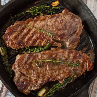 Overhead square image of 2 steaks in a cast iron pan.