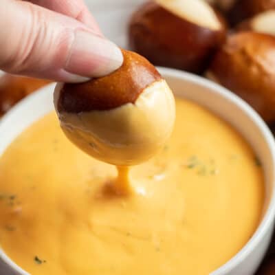 Square image of a pretzel bite being dipped into cheese dip.