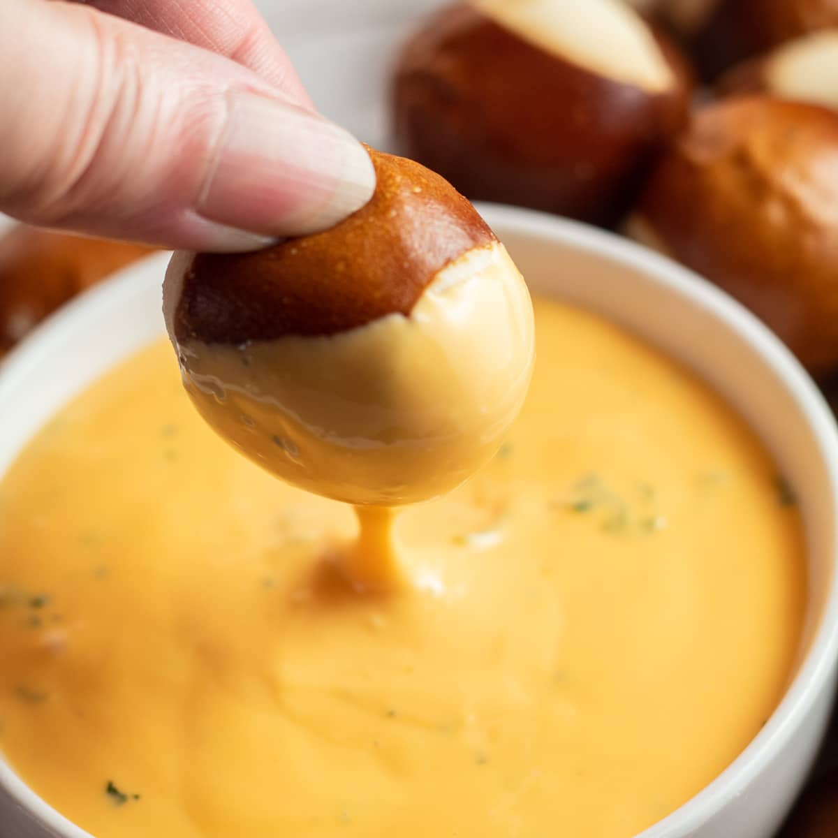 Immagine quadrata di un morso di pretzel che viene immerso nella salsa di formaggio.