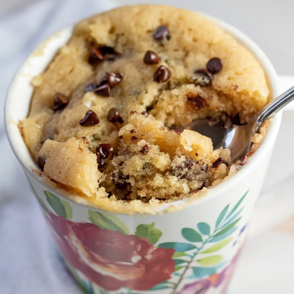 Square image of flowered mug with chocolate chip cake.