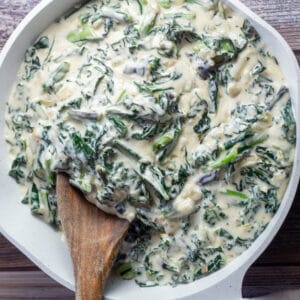 Square image of creamed kale in skillet with wooden spoon.