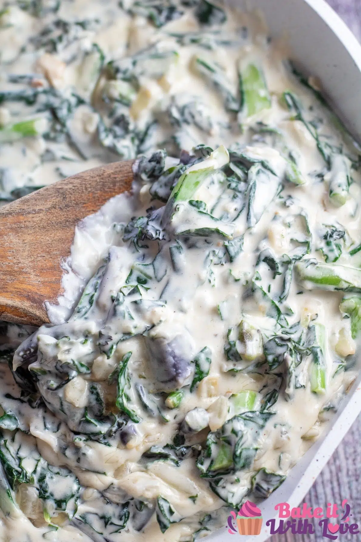 Tall image of creamed kale in skillet with wooden spoon.