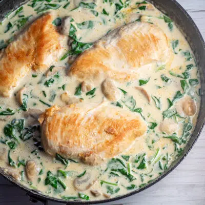 Square image of chicken in creamy Parmesan sauce in a skillet.