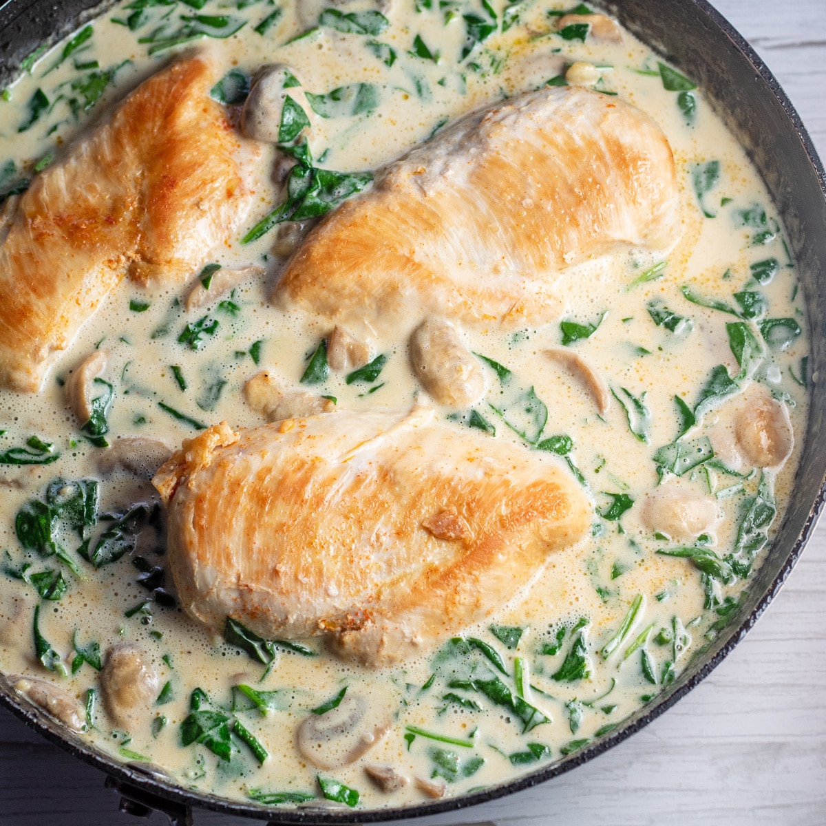 Square image of chicken in creamy Parmesan sauce in a skillet.
