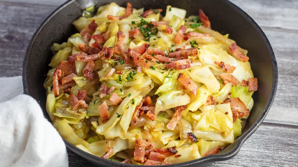 Wide image of a cast iron pan with Southern fried cabbage with bacon.