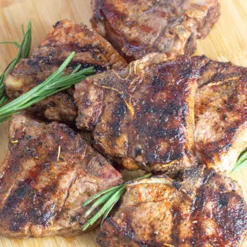 Wide image of grilled lamb chops on a wooden cutting board.