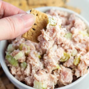 Quadratisches Bild eines Crackers, der in Schinkensalat getaucht wird.