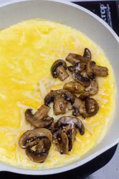 Process photo 8 showing mostly cooked egg with mushrooms on one side of omelet.
