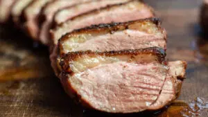 Wide image of perfectly pan seared duck breast sliced and served on wooden cutting board.