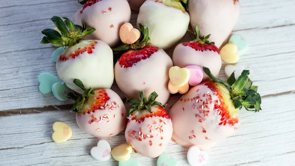 Wide closeup of the best pink chocolate covered strawberries with heart decor and conversation hearts.