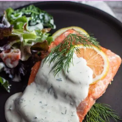 Pin image with text of salmon with dillsauce on a black plate with lemon slice.