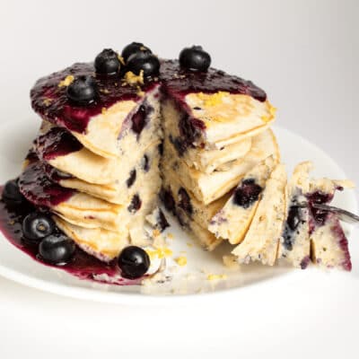 Square image of a stack of blueberry pancakes with blueberry syrup.