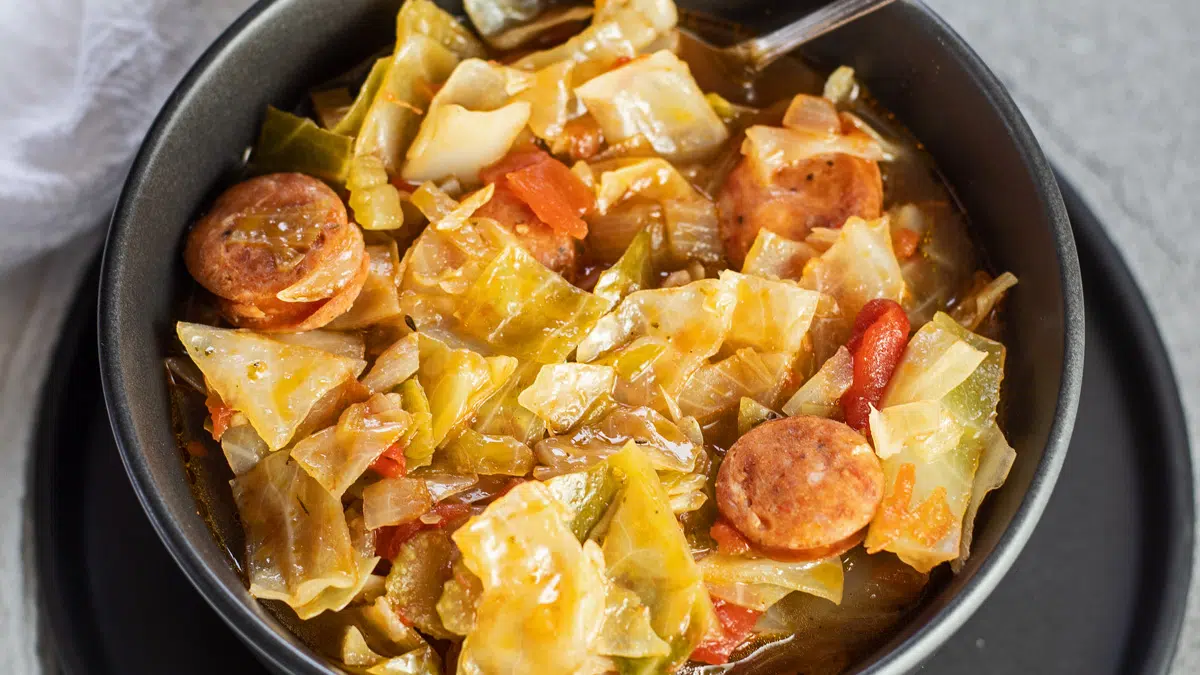 Wide image of Cajun cabbage stew in a black bowl.