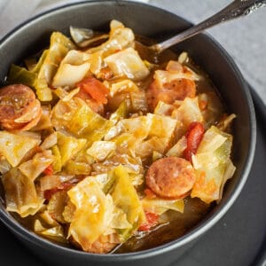 Square image of Cajun cabbage stew in a black bowl.