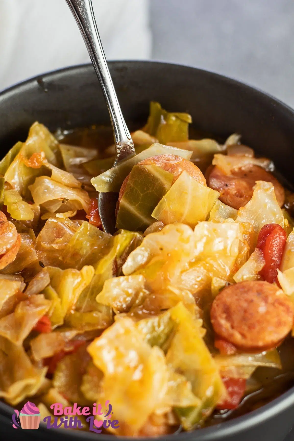 Tall image of Cajun cabbage stew in a black bowl.