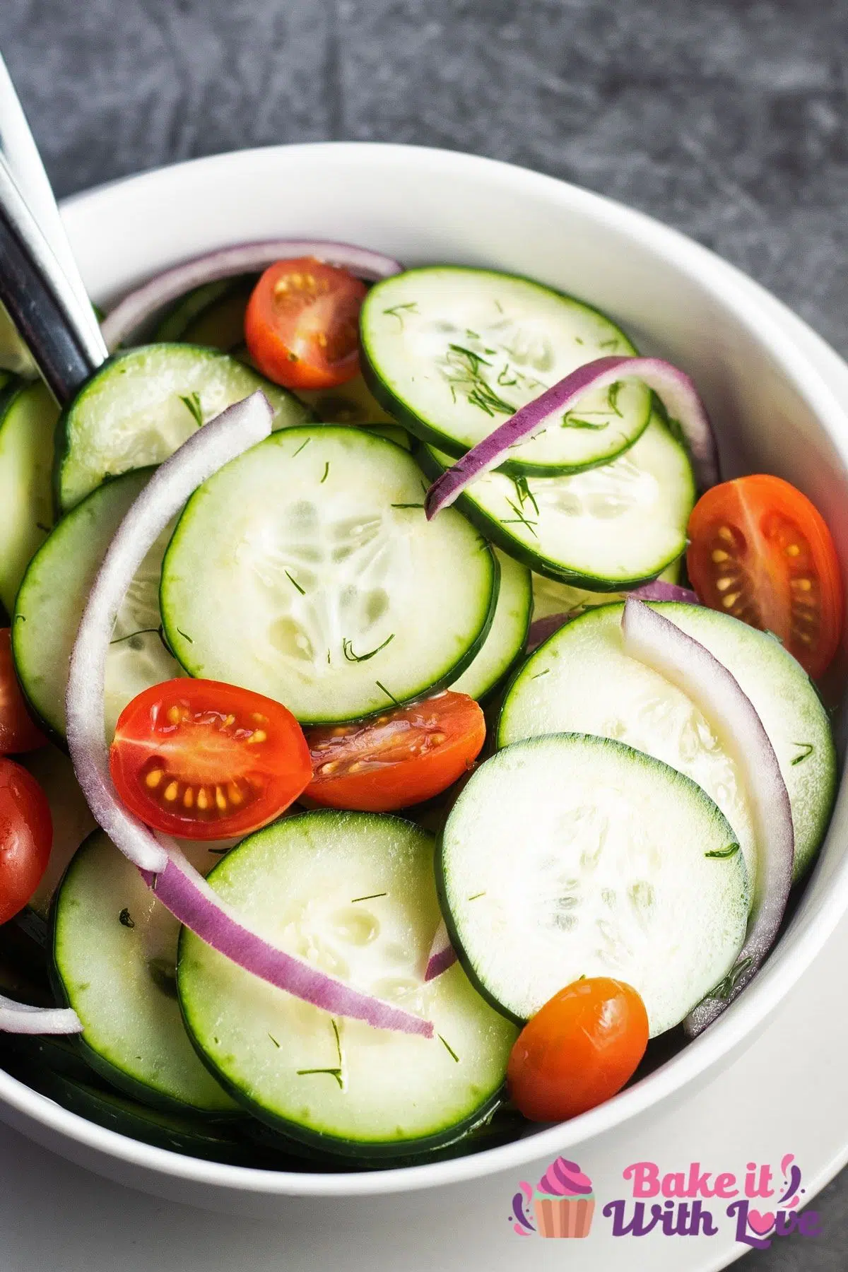 Tall image of the cucumber salad with vinegar and dill marinade tossed with red onion and halved cherry tomatoes.