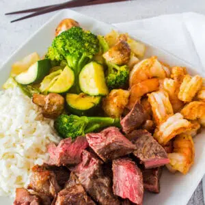 Square image of Hibachi steak and shrimp on a white plate with chopsticks.