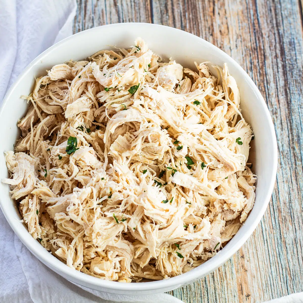 Best Instant Pot shredded chicken served in white bowl with parsley garnish on wooden background.