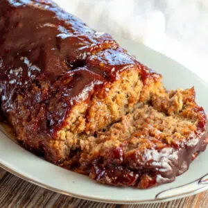 Sliced bbq meatloaf with tangy topping served on white platter.