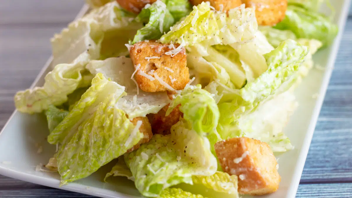 Wide closeup on the creamy Caesar salad dressing no anchovies tossed with greens and served with croutons.