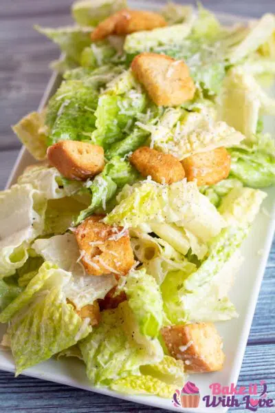 Delicious creamy caesar salad dressing tossed with romaine and croutons on white plate.