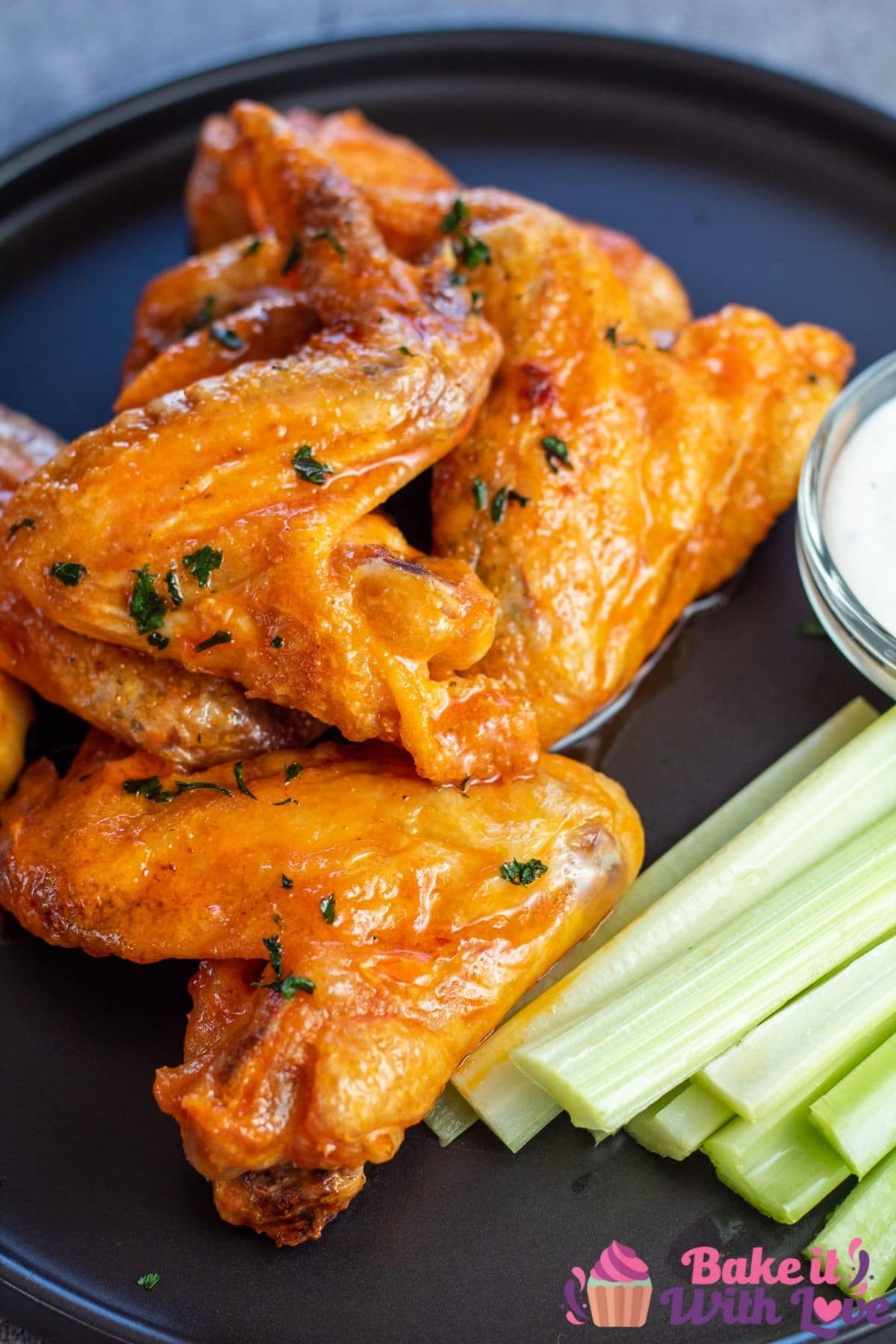 Tall image of chicken wings on a black plate with celery.