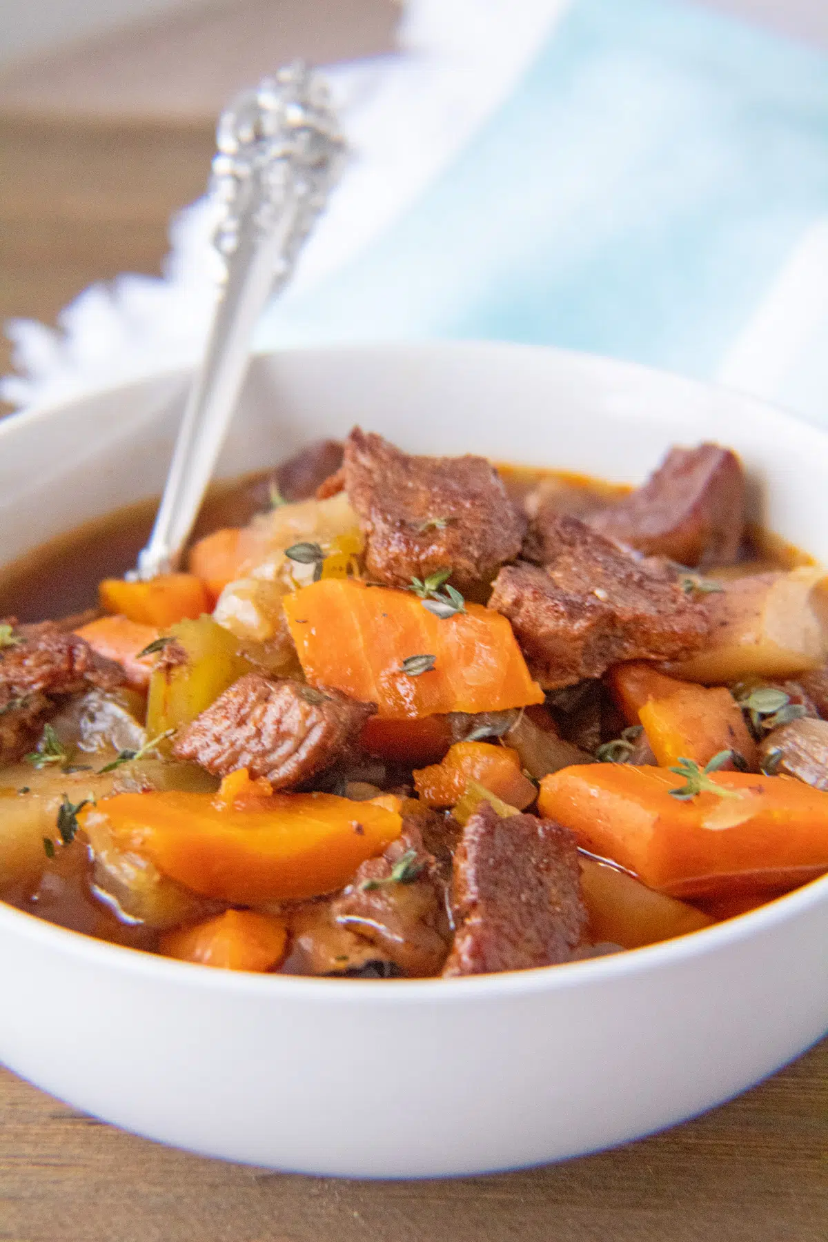 Tall image of the crockpot beef stew served in white bowl.
