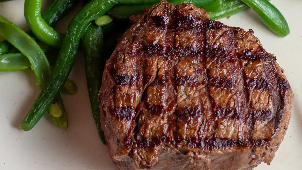 Wide image of grilled filet mignon on a plate with green beans.