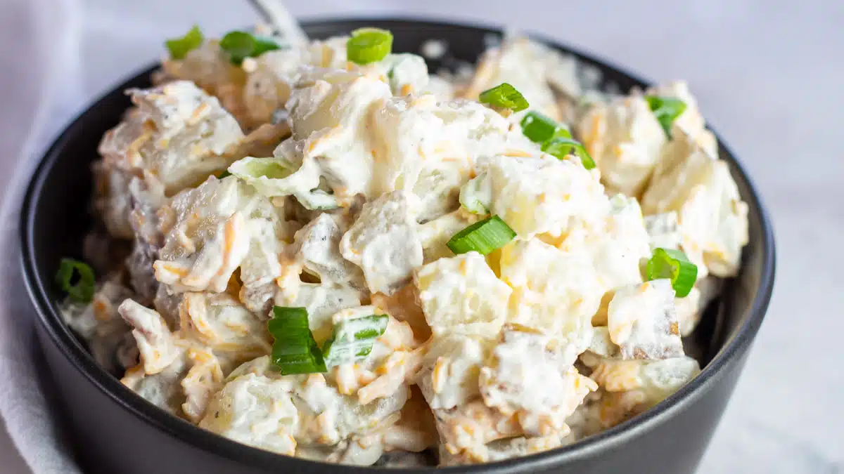 Wide closeup on the loaded baked potato salad with green onion garnish.