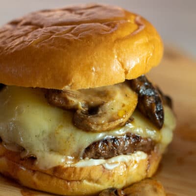 Imagem quadrada de um saboroso hambúrguer suíço de cogumelos com cogumelos salteados macios e queijo suíço derretido.