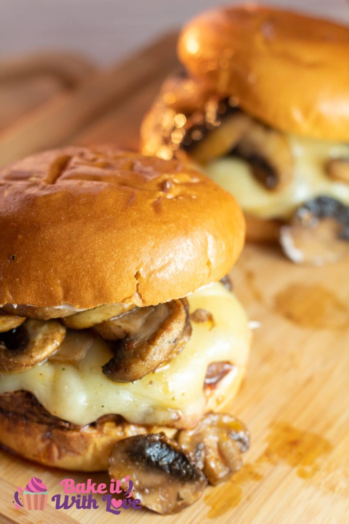 Tall image of two mushroom swiss burgers assembled on a cutting board.